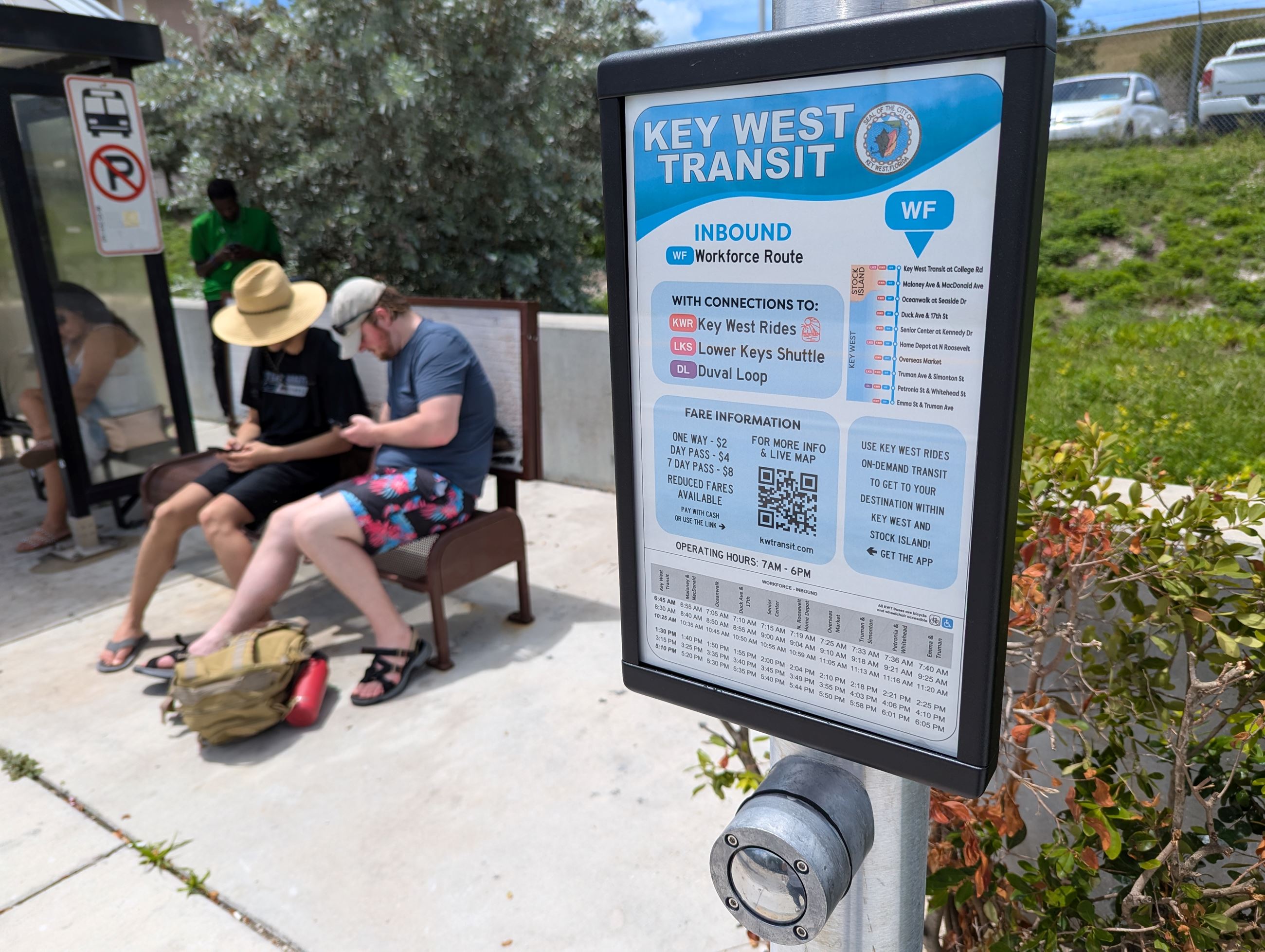 Bus stop sign mounted on a pole with people waiting for the bus in the background