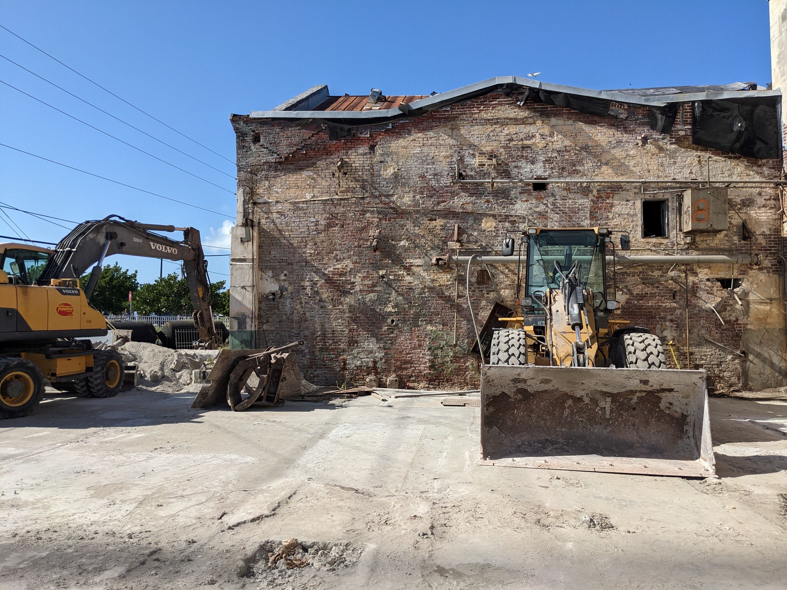 Construction equipment in front of a brick building in disrepair.